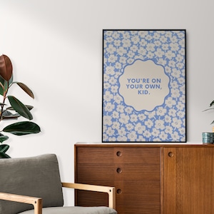 May include: A framed print with a blue background and white flowers. The print features a white speech bubble with the text "YOU'RE ON YOUR OWN, KID."