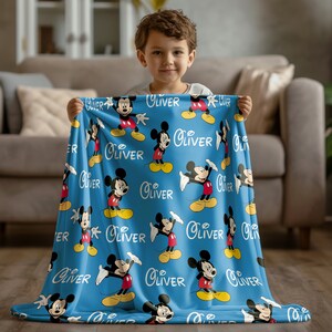 May include: A blue fleece blanket with a repeating pattern of Mickey Mouse and the name "Oliver".