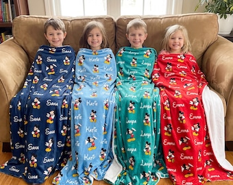 May include: Four soft fleece blankets in dark blue, light blue, teal, and red, each featuring a repeating Mickey Mouse pattern and the personalized names Sana, Katie, Lanya, and Emma printed in white script across the fabric surface.