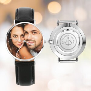 K&ouml;nnte beinhalten: Eine silberne Armbanduhr mit schwarzem Lederarmband. Das Zifferblatt zeigt ein Farbfoto eines Paares. Die R&uuml;ckseite der Uhr ist silberfarben mit dem Text "EMPEREUR NAUTIC LONDON" und einem Ankersymbol.