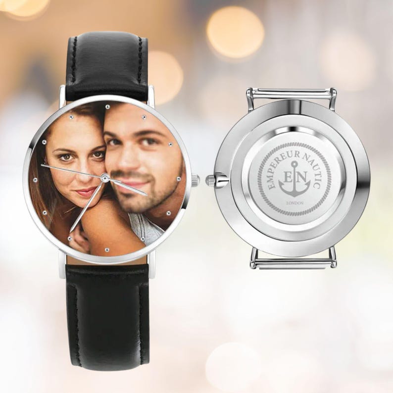 K&ouml;nnte beinhalten: Eine silberne Armbanduhr mit schwarzem Lederarmband. Das Zifferblatt zeigt ein Farbfoto eines Paares. Die R&uuml;ckseite der Uhr ist silberfarben mit dem Text "EMPEREUR NAUTIC LONDON" und einem Ankersymbol.