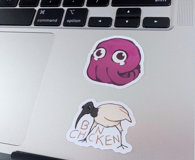 K&ouml;nnte beinhalten: Zwei Aufkleber auf einem Laptop. Einer ist ein Cartoon-Oktopus in Rosa mit gro&szlig;en Augen. Der andere ist ein Cartoon-Vogel mit dem Text "BIN CHICKEN".