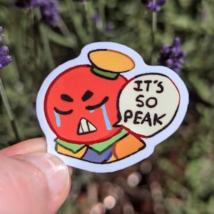 Puede incluir: Una pegatina con un personaje de dibujos animados con una cabeza roja, un sombrero amarillo y un cuerpo naranja. El personaje tiene una expresión triste con lágrimas y un bocadillo que dice "IT'S SO PEAK".