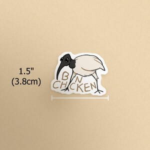 K&ouml;nnte beinhalten: Aufkleber mit einem Cartoon-Ibis-Vogel mit schwarzem Kopf und Schnabel und wei&szlig;em K&ouml;rper. Der Text "BAN CHICKEN" steht unter dem Vogel. Der Aufkleber ist 3,8 cm lang.