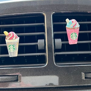 May include: Four colorful car air freshener charms shaped like Starbucks Frappuccinos. The charms are pink, blue, green, and yellow with glitter and a white Starbucks logo.