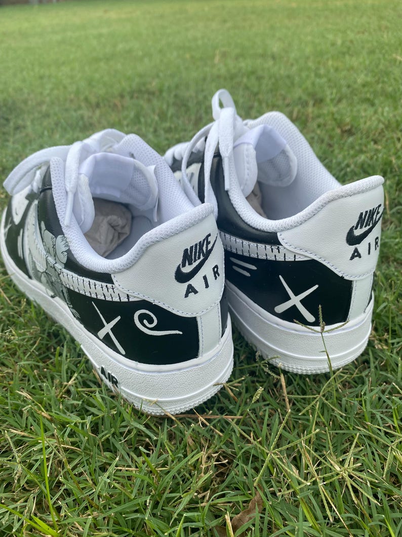 Peut inclure: Paire de baskets Nike Air Force 1 noires et blanches avec des motifs personnalis&eacute;s. Les chaussures ont des lacets, des semelles et des languettes de talon blancs avec le logo Nike Air. Les c&ocirc;t&eacute;s pr&eacute;sentent un motif floral et la lettre "X" et un tourbillon.