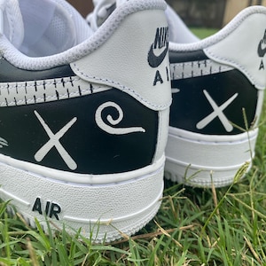 Peut inclure: Gros plan sur deux baskets blanches et noires avec des motifs personnalis&eacute;s. Les baskets ont une semelle et des accents blancs, avec des d&eacute;tails noirs sur le talon et les c&ocirc;t&eacute;s. Le mot "AIR" est visible sur la semelle.