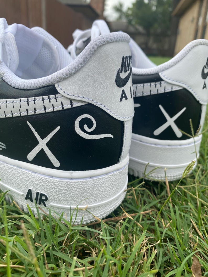 Peut inclure: Gros plan sur deux baskets blanches et noires avec des motifs personnalis&eacute;s. Les baskets ont une semelle et des accents blancs, avec des d&eacute;tails noirs sur le talon et les c&ocirc;t&eacute;s. Le mot "AIR" est visible sur la semelle.