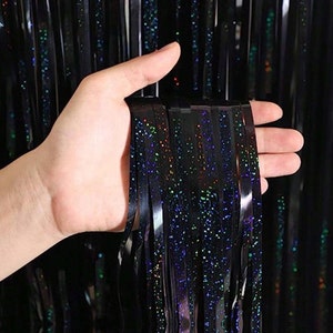 Może przedstawiać: Czarna, tęczowa zasłona z frędzli z folii z ręką trzymającą część frędzli. Frędzle są wykonane z cienkich pasków folii z błyszczącym wykończeniem.