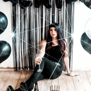 May include: A black and white photo of a woman celebrating her 30th birthday with black balloons that spell out "RIP Twenties".