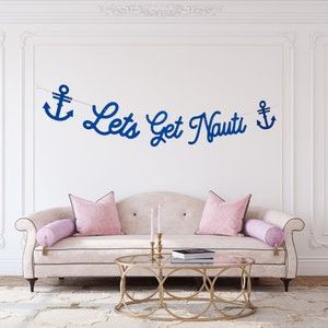 Puede incluir: Un sof&aacute; blanco con cojines rosas y una mesa de centro de metal dorado. Un banner azul con anclas y el texto "Let's Get Nauti" cuelga en la pared detr&aacute;s del sof&aacute;.