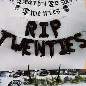 May include: Black and white party decorations with the text "Death to My Twenties" and "RIP Twenties". The decorations include a banner, balloons, and plates.
