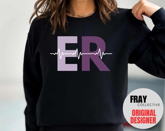 May include: Black sweatshirt with a purple and light purple "ER" graphic with a white heartbeat line above it. The text "FRAY COLLECTIVE ORIGINAL DESIGNER" is visible in the lower right corner.
