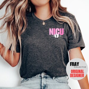 Pu&ograve; includere: Una maglietta grigio scuro con una grafica rosa che dice "NICU" con una linea di battito cardiaco e impronte di piedi di bambino rosa. Il testo "FRAY COLLECTIVE ORIGINAL DESIGNER" &egrave; su un cerchio bianco nell'angolo in basso a destra dell'immagine.