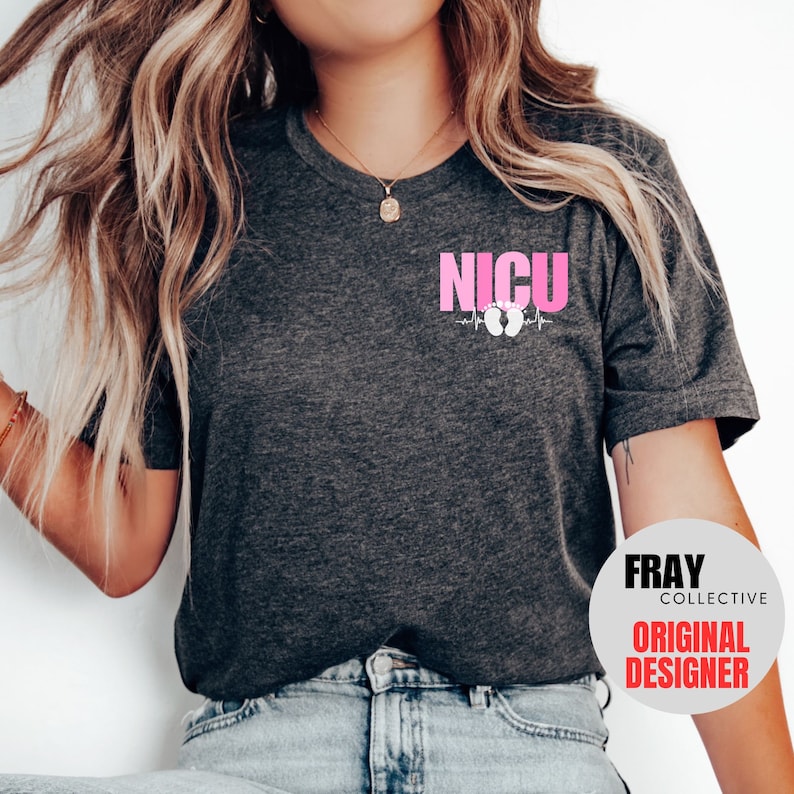 Pu&ograve; includere: Una maglietta grigio scuro con una grafica rosa che dice "NICU" con una linea di battito cardiaco e impronte di piedi di bambino rosa. Il testo "FRAY COLLECTIVE ORIGINAL DESIGNER" &egrave; su un cerchio bianco nell'angolo in basso a destra dell'immagine.