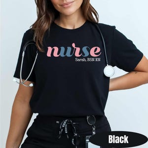 May include: Black t-shirt with the word "nurse" in pink and blue lettering. Below the word "nurse" is the text "Sarah, BSN RN". A stethoscope hangs around the neck. The word "Black" is in a black oval at the bottom.