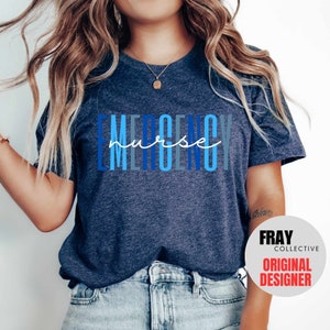 Puede incluir: Una camiseta azul oscuro con el texto "EMERGENCY nurse" en letras azules y blancas. El texto est&aacute; apilado verticalmente con la palabra "nurse" escrita en cursiva.