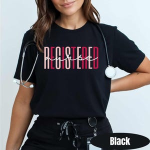 May include: Black t-shirt with the words "REGISTERED nurse" in a pink and red design. A stethoscope hangs around the neck. The shirt is a crew neck and has short sleeves.
