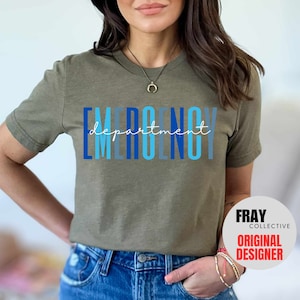 May include: A green t-shirt with the text "EMERGENCY department" in blue and light blue lettering. The text is stacked vertically with the word "department" in a smaller font size and written in cursive. The t-shirt is being worn by a person. The image also includes a white circle with the text "FRAY COLLECTIVE ORIGINAL DESIGNER" in black text.