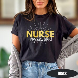 May include: Black t-shirt with the word "NURSE" in gold block letters, and the phrase "HAPPY NEW YEAR!" in white. The design includes a starburst pattern. The shirt is paired with blue jeans.