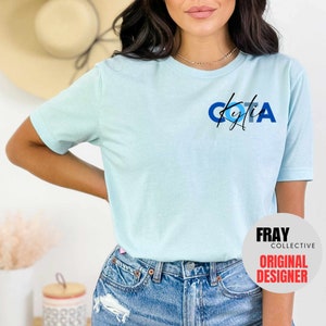May include: A light blue t-shirt with a blue, white, and black graphic that says "COTA Kylie". The shirt is made of a soft, comfortable material and has a relaxed fit.