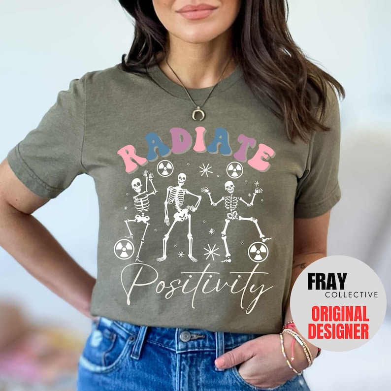 May include: A green t-shirt with a graphic of three skeletons dancing with the text "RADIATE POSITIVITY" in a rainbow color scheme. The text "FRAY COLLECTIVE ORIGINAL DESIGNER" is in a white box in the lower right corner.
