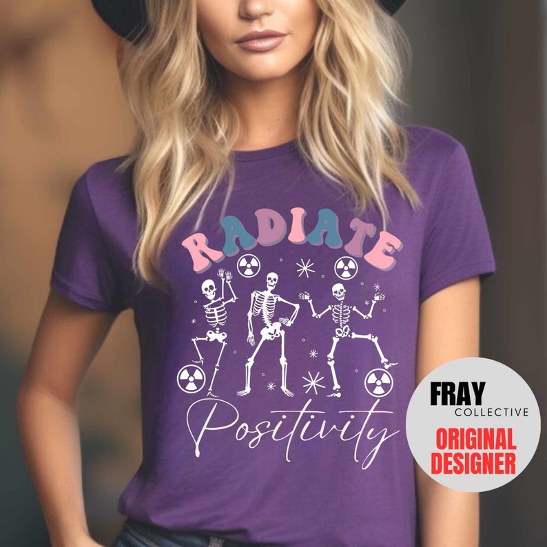 May include: Purple t-shirt with a white graphic of three skeletons dancing with the text "RADIATE POSITIVITY" in pink, blue, and white. The graphic also includes three white radiation symbols.
