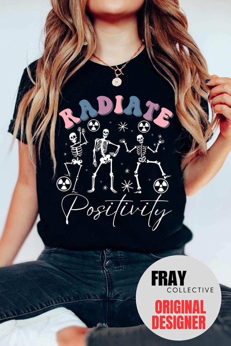 May include: Black t-shirt with a graphic of three skeletons dancing with the text "RADIATE POSITIVITY" in pink, blue, and purple letters. The skeletons are holding radiation symbols.