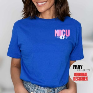 Pu&ograve; includere: Una t-shirt blu reale con il testo "NICU" in lettere rosa e una grafica di impronta di piede rosa con una linea di battito cardiaco. Il testo "FRAY COLLECTIVE ORIGINAL DESIGNER" &egrave; in lettere bianche su un cerchio nero nell'angolo in basso a destra dell'immagine.