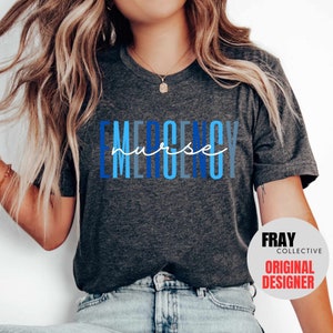 Puede incluir: Una camiseta gris oscuro con el texto "EMERGENCY nurse" en letras azules y blancas. El texto est&aacute; apilado verticalmente con la palabra "nurse" en una fuente cursiva. La camiseta la lleva puesta una persona con el pelo largo y rubio. El texto "FRAY COLLECTIVE ORIGINAL DESIGNER" es visible en la esquina inferior derecha de la imagen.