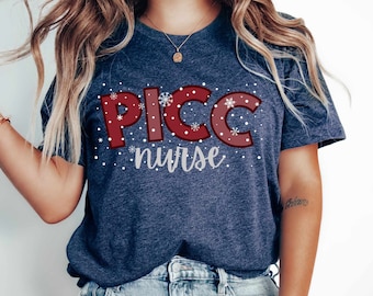 May include: A navy blue t-shirt with a red and white design that says "PICC nurse" with snowflakes around the text.