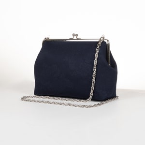 May include: A dark blue fabric clutch bag with a silver chain strap and a silver clasp.