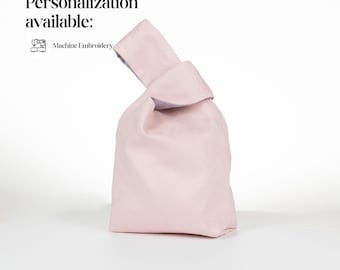 May include: A light pink knot bag with a single handle loop. The text Personalization available: Machine Embroidery is visible in the upper left corner. The bag features a soft, solid-colored fabric construction with a simple, minimalist silhouette.