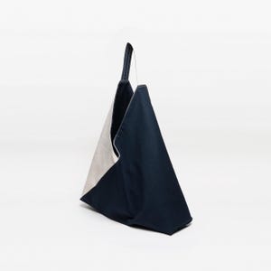 May include: A navy blue and beige tote bag with a single handle. The bag is made of a sturdy fabric and has a geometric design. The interior of the bag is beige, while the exterior is navy blue.