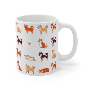 May include: White ceramic mug with a pattern of Shiba Inu dogs in various poses. The dogs are in shades of brown, black, and white. There is a small red heart in the center of the mug.