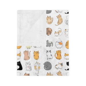 May include: A white fleece blanket featuring a pattern of colourful cartoon cats in various poses. The cats are all different colours and have different expressions.