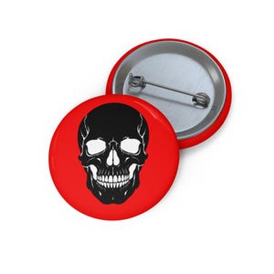 May include: A round pin-back button featuring a vibrant red background with a high-contrast black and white graphic of a human skull centered on the front. The back of the button is metallic silver with a standard pin fastener attached.