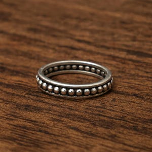 May include: A silver ring with a beaded design. The ring features two bands of small, evenly spaced beads around the circumference. The ring is set against a dark wood surface.
