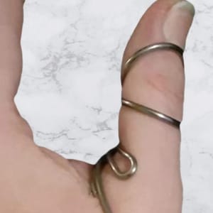 May include: A silver metal thumb splint with a spiral design. The splint is wrapped around a person's thumb.