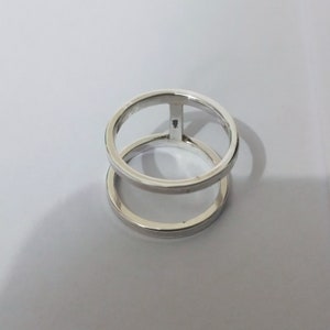 以下が含まれることがあります： 二重の円のデザインが施された銀の指輪。指輪は2つの円からなり、1つの円がもう1つの円の中にあります。内側の円は外側の円よりも少し小さいです。