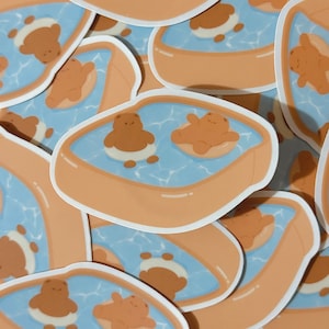 May include: Two brown bears are floating in a blue pool with a brown inflatable ring. The pool is surrounded by a brown inflatable rim. The bears are wearing white swimsuits.
