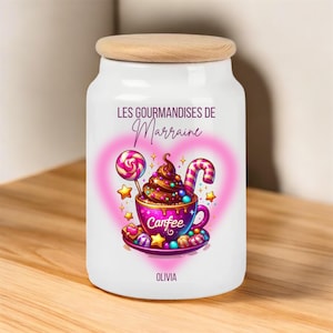 Peut inclure: Pot en céramique blanche avec un couvercle en bois. Le pot a un motif de cœur rose avec une image de dessin animé d'un milk-shake au chocolat avec des bonbons et une sucette. Le texte sur le pot est "Les Gourmandises de Marraine Olivia".