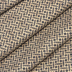Puede incluir: Primer plano de tela beige con un patr&oacute;n repetido de dise&ntilde;os florales y de hojas azul marino. La tela est&aacute; doblada, mostrando las variaciones de textura y patr&oacute;n. Ideal para acolchar o manualidades.