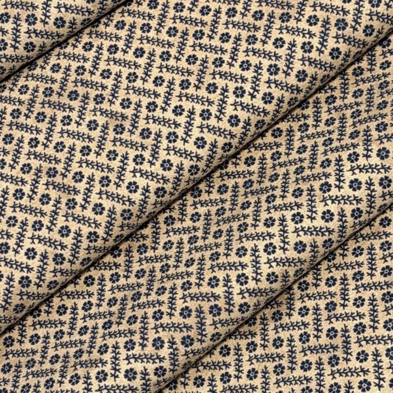 Puede incluir: Primer plano de tela beige con un patr&oacute;n repetido de dise&ntilde;os florales y de hojas azul marino. La tela est&aacute; doblada, mostrando las variaciones de textura y patr&oacute;n. Ideal para acolchar o manualidades.