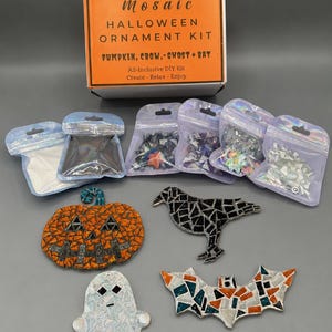 May include: A Mosaic Halloween Ornament Kit box with text reading Mosaic Halloween Ornament Kit Pumpkin, Crow, Ghost + Bat. Below are four small finished mosaic ornaments: an orange pumpkin, a black crow, a white ghost, and a multi-colored bat.