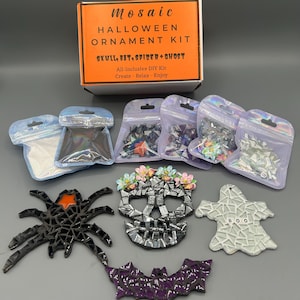 May include: A Halloween mosaic ornament kit in an orange and white box labeled Mosaic Halloween Ornament Kit Skull, Bat, Spider + Ghost. Includes four small iridescent bags of mosaic tiles and four finished ornaments: a black spider, a skull with flowers, a purple bat, and a white ghost with the word BOO.