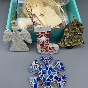 May include: A collection of mosaic Christmas ornaments, including an angel, a stocking, a bell, and a snowflake. The ornaments are made of various colored glass pieces. A craft kit box is visible in the background.