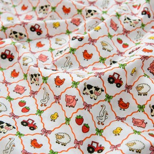 Peut inclure: Un tissu blanc avec un motif répétitif en losanges délimité par des lignes orange et des nœuds verts à chaque intersection. L'imprimé présente des illustrations de vaches, cochons, moutons, poules, poussins, oies, tracteurs rouges et fraises.