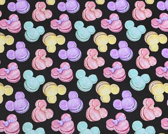 May include: A repeating pattern of colorful macarons in the shape of a mouse head and bow on a black background. The macarons are in pastel shades of pink, purple, yellow, and blue.