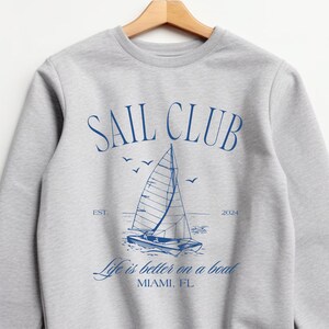 May include: Grey sweatshirt with a blue graphic of a sailboat and the text "SAIL CLUB EST. 2004 Life is better on a boat MIAMI, FL"